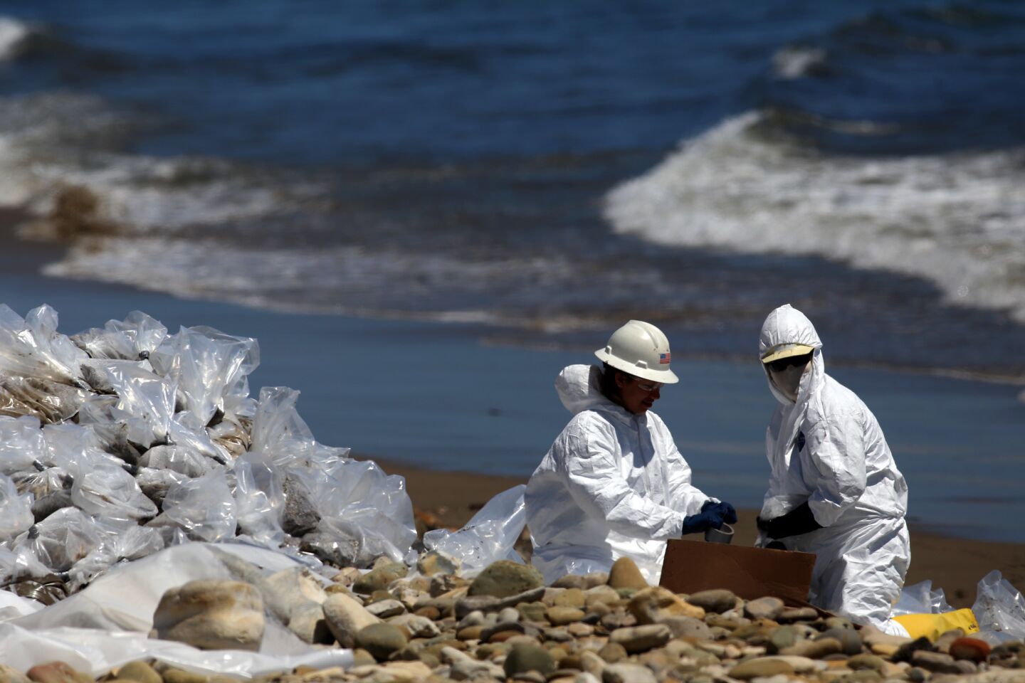 Suited cleanup workers bag oiled sand and rocks on the shoreline at Refugio State Beach near Santa Barbara.