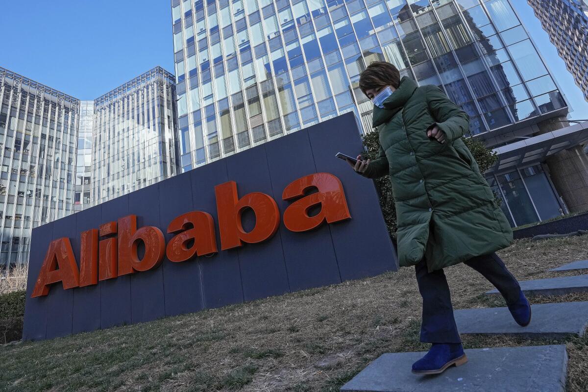 FILE - A woman walks past the offices of Chinese e-commerce firm Alibaba in Beijing on Dec. 13, 2021. Alibaba Group Holding on Thursday, Aug. 4, 2022, beat market expectations for revenue in its quarter ended June, even as revenue was nearly flat and the company continues to grapple with the fallout from increased regulatory scrutiny and slowing economy growth. (AP Photo/Andy Wong, File)