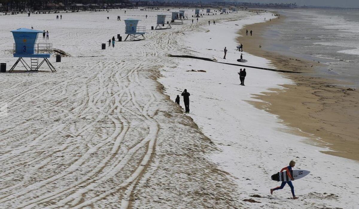 A surfer runs across hail-covered sand in Huntington Beach.