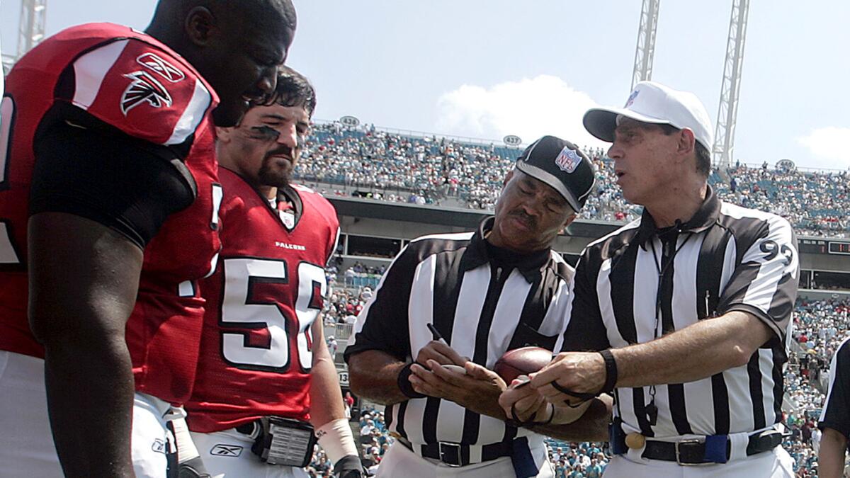 NFL referee Tony Corrente (99) shows Falcons captains the coin he will toss as official Don Carey prepares to write down their call of 'heads' or tails' before a game against the Jaguars earlier this season.