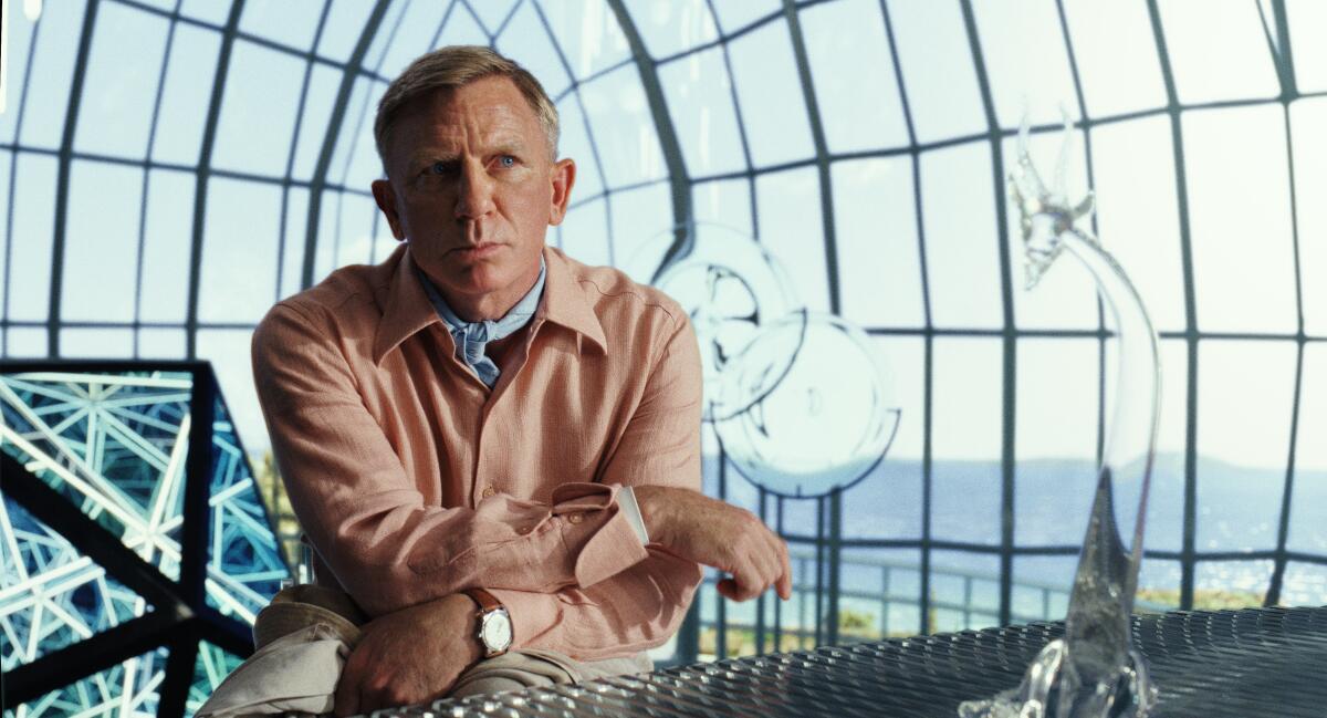 A man in a pink suit sitting at a table in a glass room