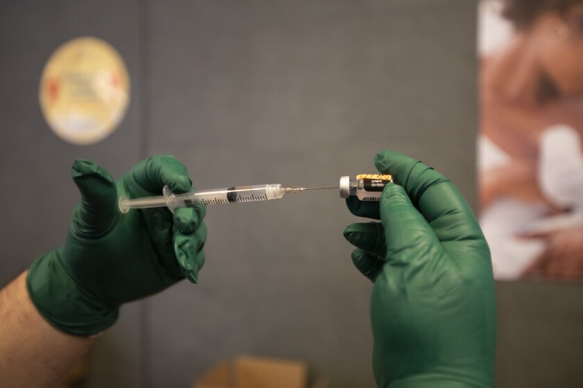 Gloved hands insert a syringe into a COVID-19 vaccine bottle