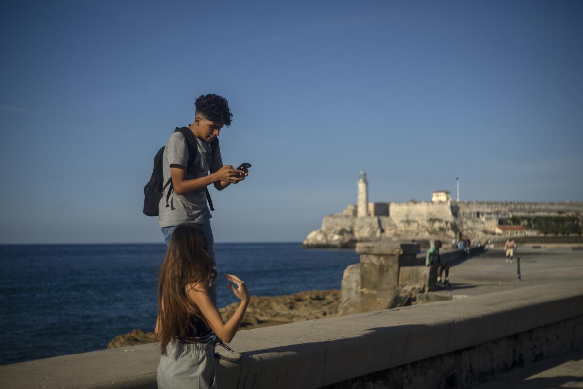 A young man looks at his phone while walking in Havana with a friend