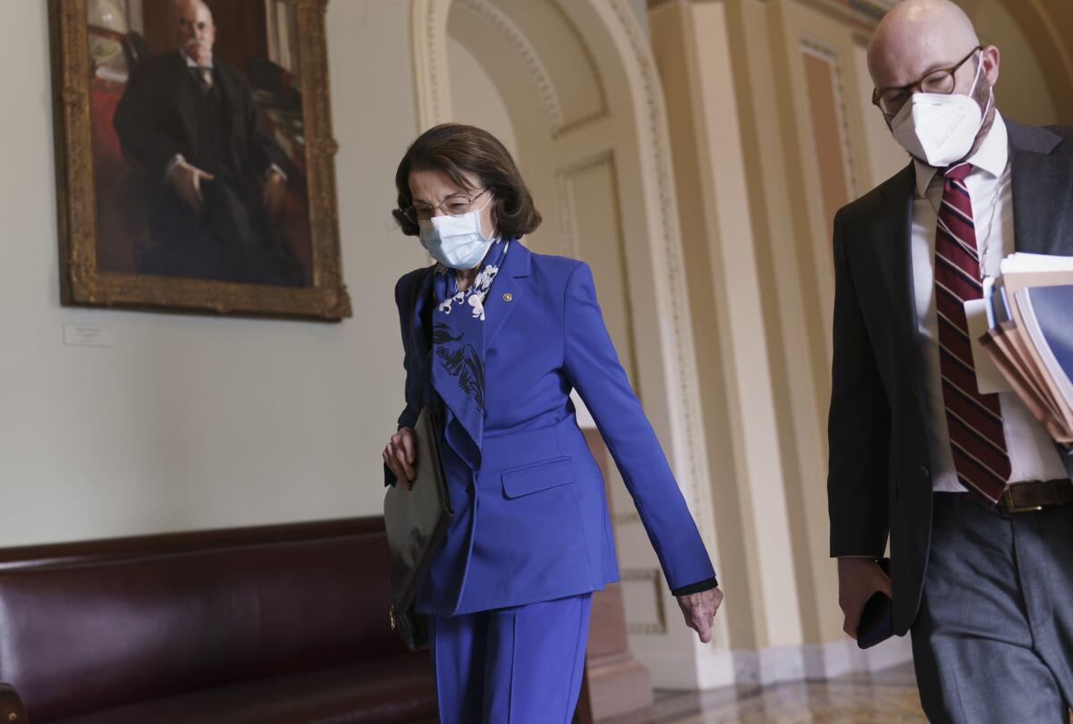 A masked Sen. Dianne Feinstein, left, walks next to an unidentified man.