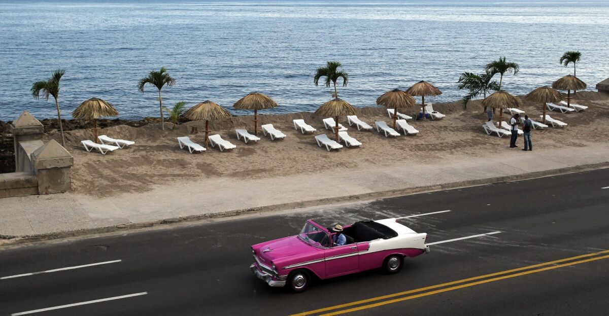 A car passes in front of an installation titled "Resaca" by Cuban artist Arles del Rio, part of the 12th Havana Biennial in Cuba. The artist transformed a patch of boardwalk into a beach.