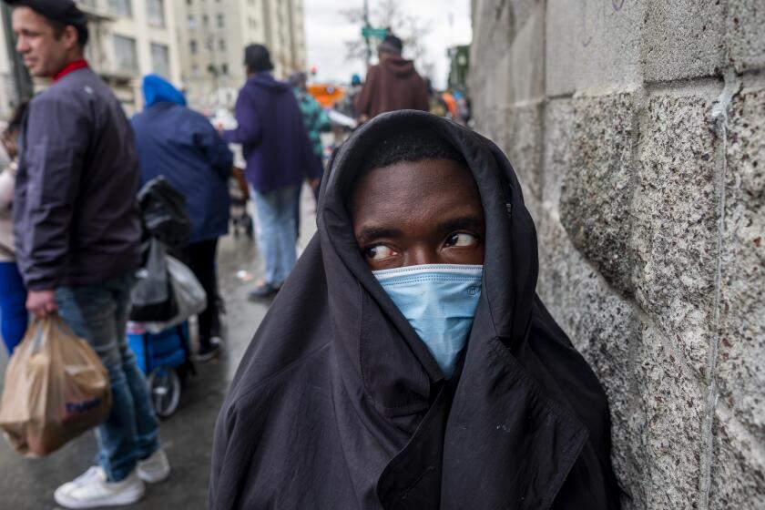 LOS ANGELES, CA - DECEMBER 25: A young man kneels next to the wall as people stand in line to receive a Christmas meal and a hygiene kits from voluteers in skidrow at The Midnight Mission on Christmas Day on Saturday, Dec. 25, 2021 in Los Angeles, CA. (Francine Orr / Los Angeles Times)