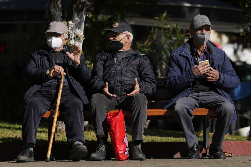 Tres ancianos con mascarillas para combatir los contagios de coronavirus, sentados en un banco en Atenas