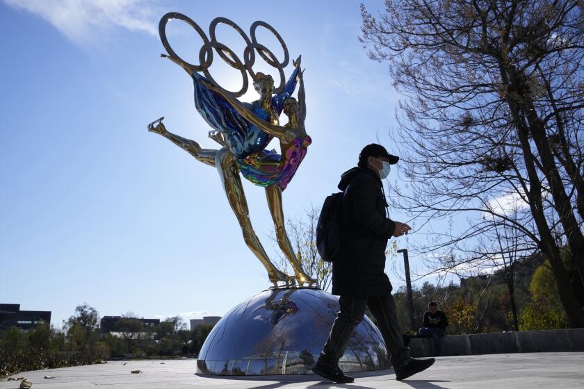 A visitor to the Shougang Park walks past the a sculpture for the Beijing Winter Olympics in Beijing, China, Tuesday, Nov. 9, 2021. China on Monday, Dec. 6, 2021, threatened to take "firm countermeasures" if the U.S. proceeds with a diplomatic boycott of February's Beijing Winter Olympic Games. (AP Photo/Ng Han Guan)