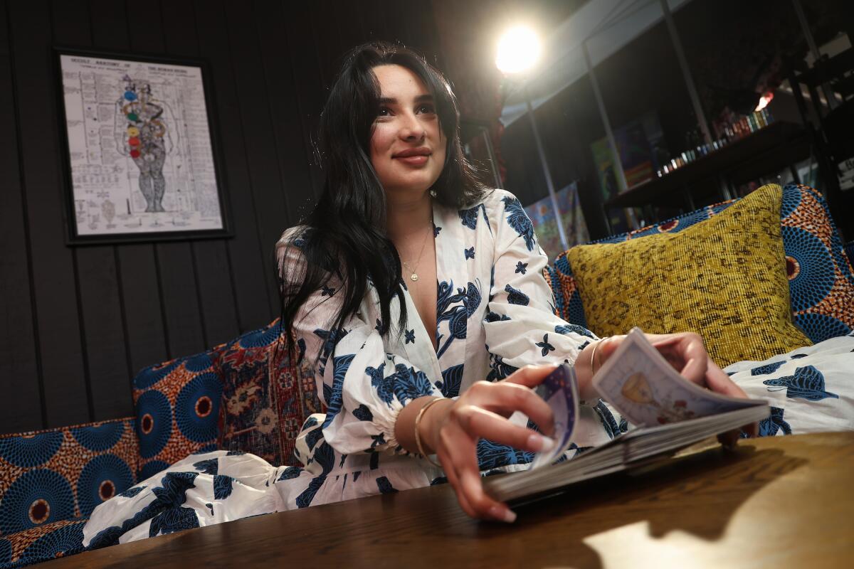 A woman with long dark hair sits and shuffles tarot cards