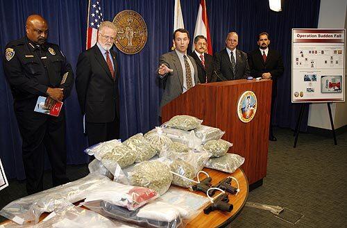 San Diego County Deputy Dist. Atty. Damon Mosler, at lectern, chief of the district attorney's narcotics division, points to the guns and drugs seized during the arrest of 96 people, including 75 students at San Diego State, on drug charges after an extensive undercover investigation called Operation Sudden Fall.