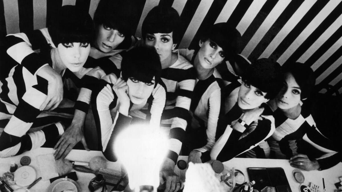 A black-and-white photo of models with short hair in black-and-white outfits looking up at a bare lightbulb