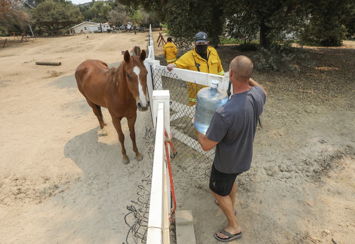 Clint Ganus holds open a gate for Pierre Nowak, who was bringing water for his horse in Lawson Valley on Wednesday.