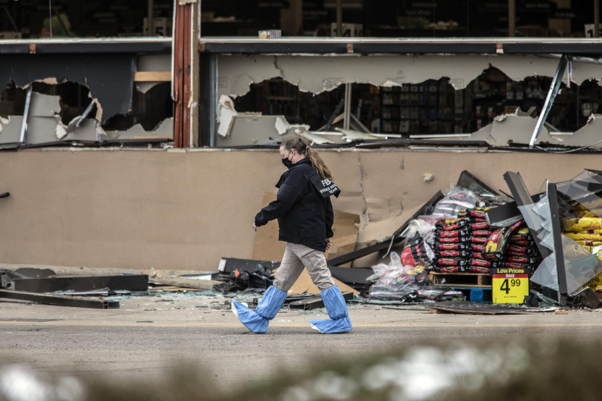 A crime scene technician in protective gear walks past the front of the King Soopers store, whose windows are all smashed