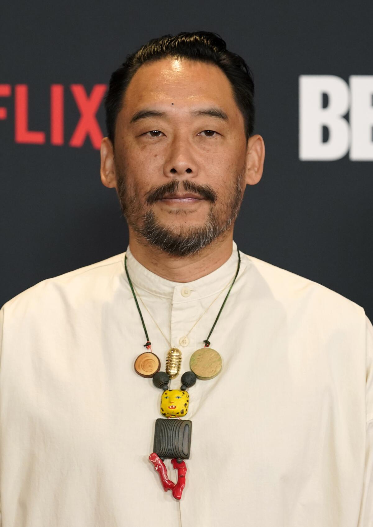 David Choe in an abstract necklace and white tunic at the "Beef" premiere