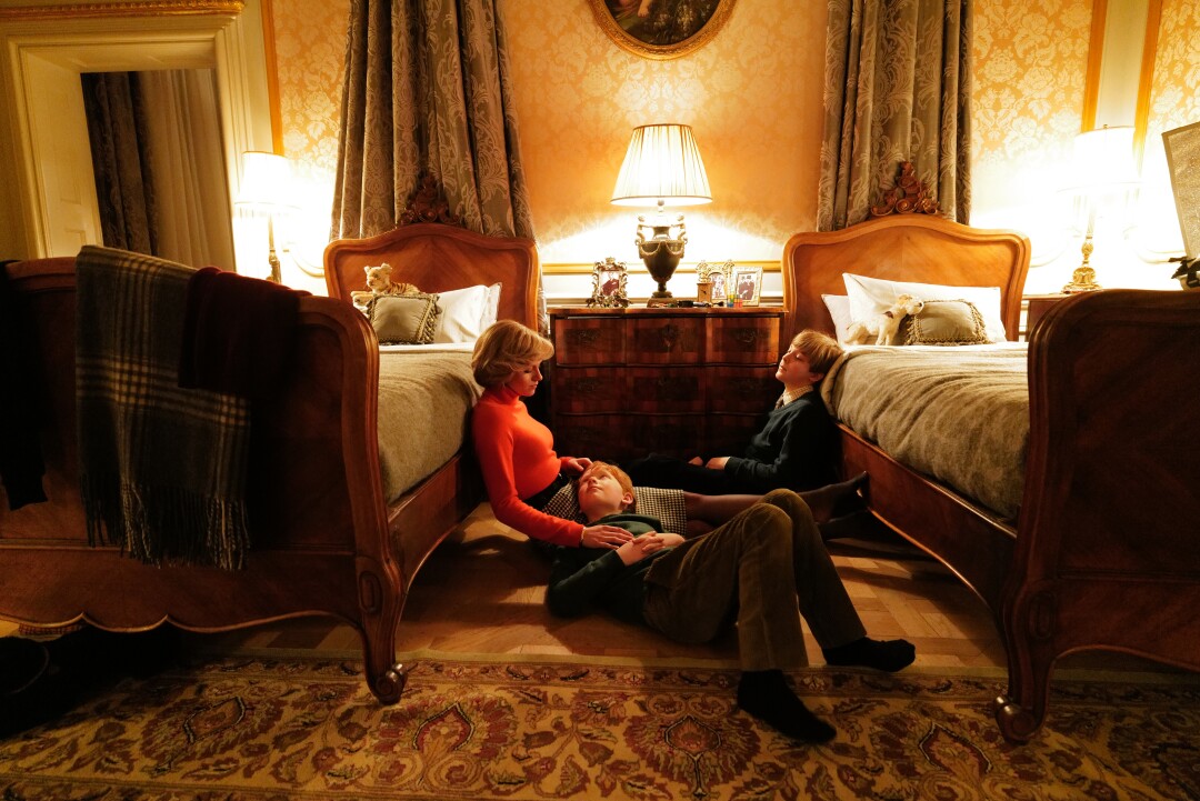 A woman and two young boys sit on the floor between twin beds.
