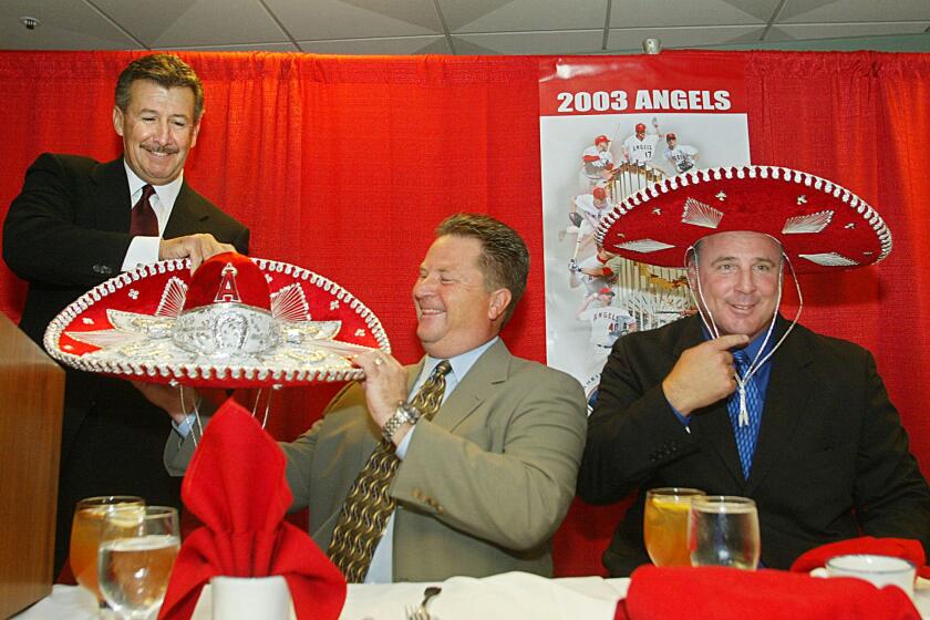 Arturo "Arte" Moreno (L) presents a gift of a sombrero with the signature "A" of the Anaheim Angeles to Angels Senior Vice-President of Businness Operations Kevin Uhlich (C) as team manager Mike Scioscia (R) tries his on during a press conference officially announcing Moreno as the new owner of the Angels, 22 May 2003, at Edison Field in Anaheim, CA. The Phoenix-based businessman is the first Latino owner of a major league team. AFP PHOTO/Lee CELANO (Photo by LEE CELANO / AFP) (Photo credit should read LEE CELANO/AFP via Getty Images)
