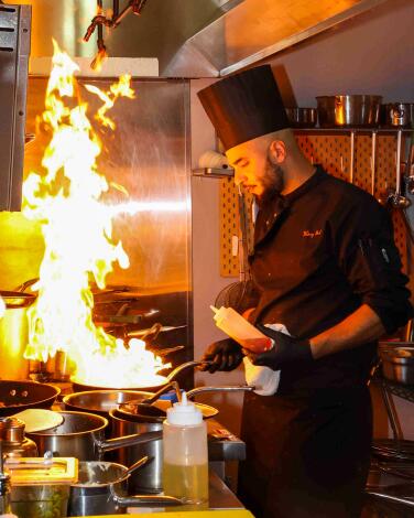A chef in a top hat flames a dish at a restaurant.