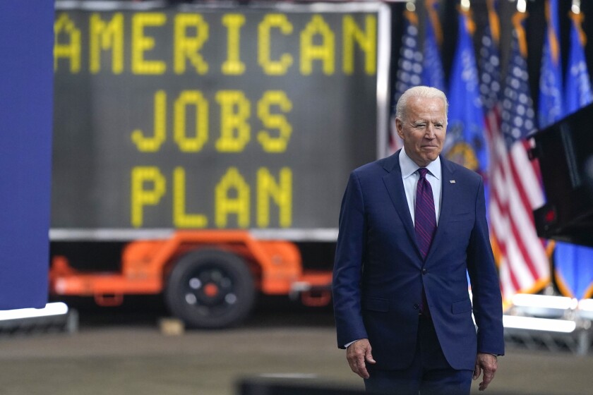 President Biden in a suit in front of a sign saying American Jobs Plan