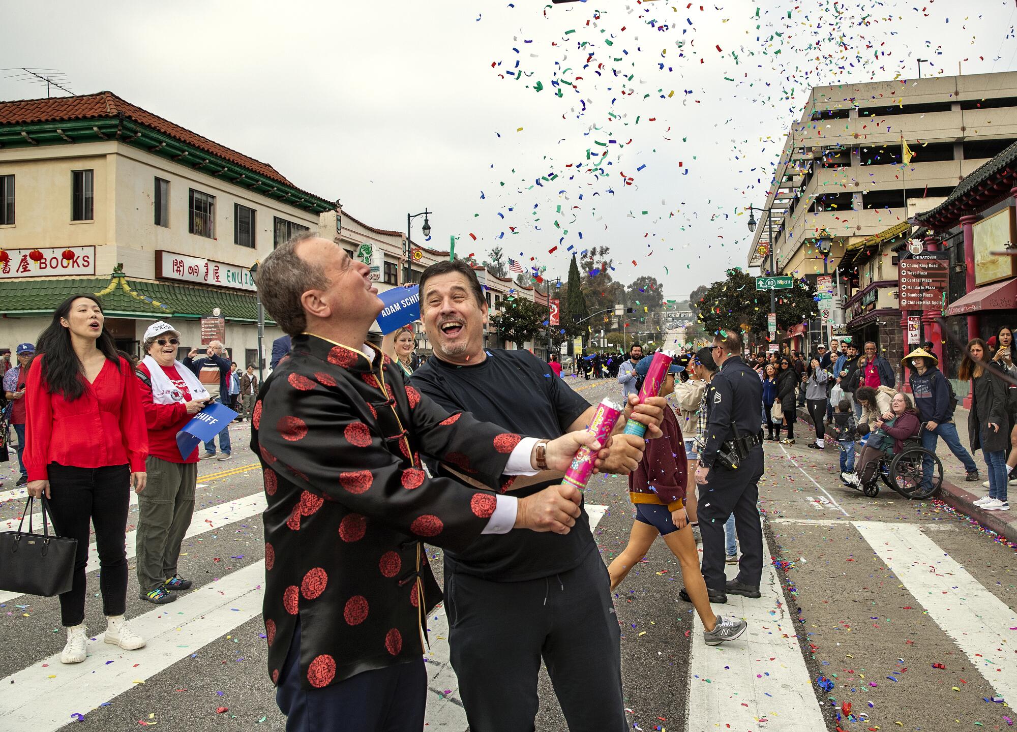 Adam Schiff, in a Chinese jacket, releases confetti into the air from a tube with another man in the street as others watch