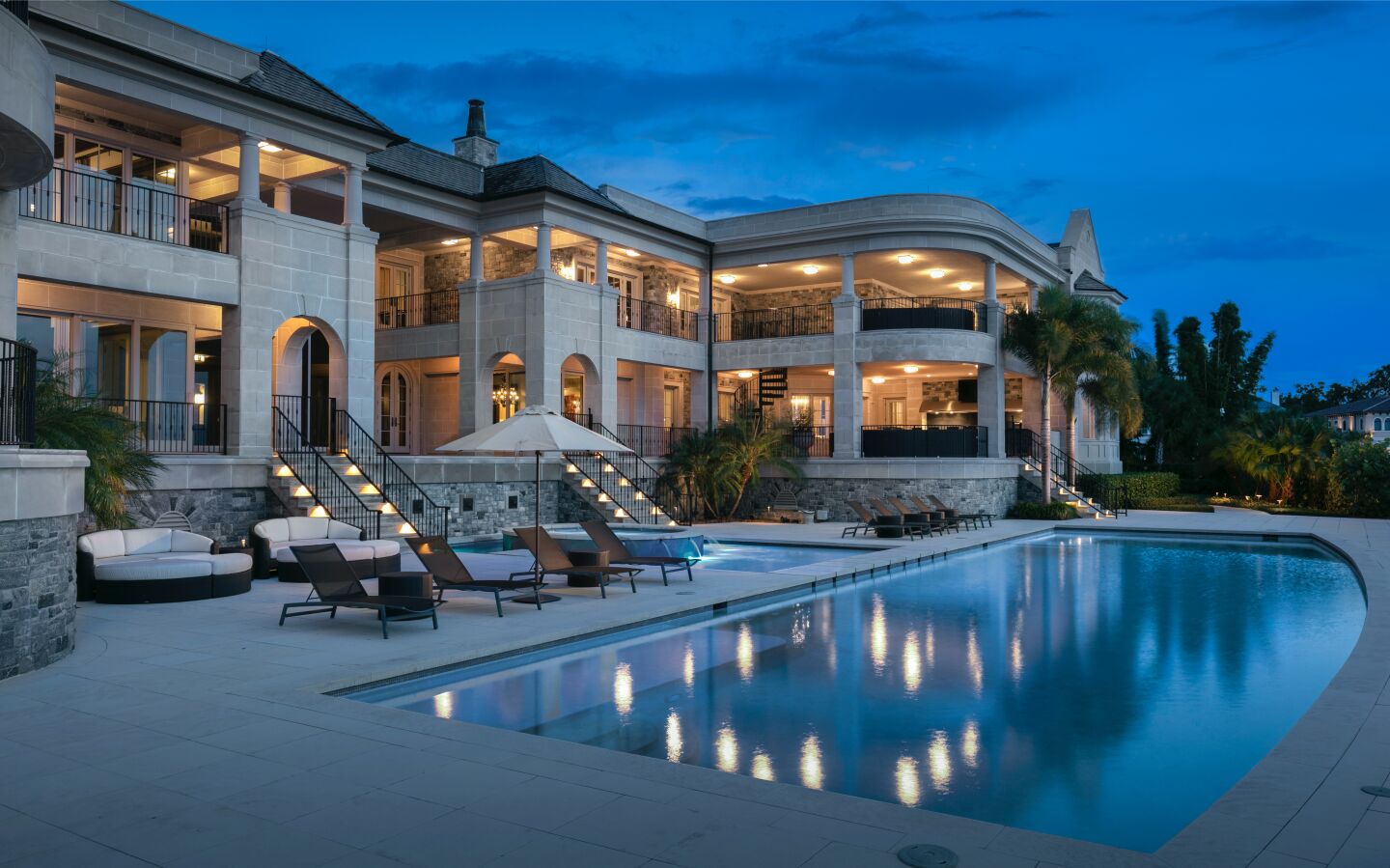 Nighttime view of the rea of the home and pool with balconies lighted up.