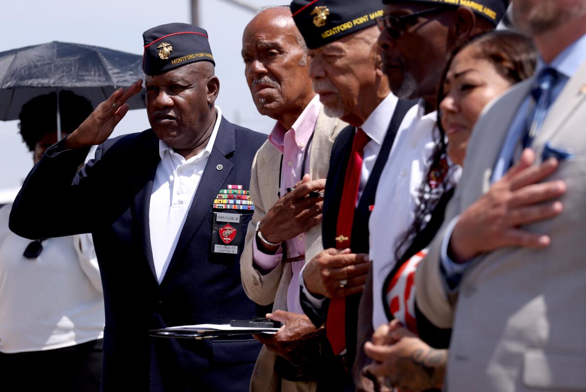 Marine veteran Charles Cook Jr., left, salutes in uniform as others stand for the National Anthem