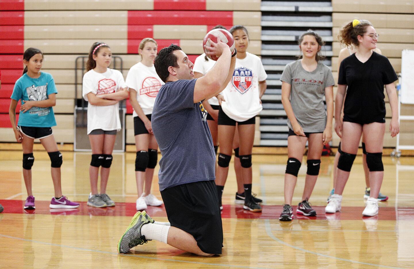 Burroughs volleyball coach Joel Brinton kneels and sets the ball to demonstrate a drill for his volleyball campers at Real's Youth Volleyball Camps at Burroughs High School on Monday, June 4, 2018.