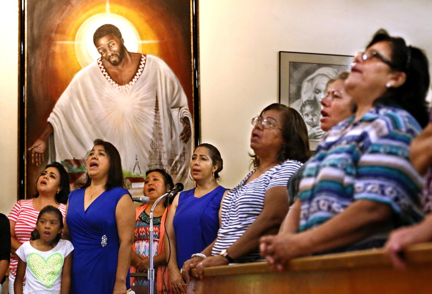 Members of St. Lawrence Brindisi Church on Compton Avenue in Watts sing during Sunday morning Mass on July 26, 2015. In the background is a painting known as "Jesus of Watts" that was donated to the church some 20 years ago.