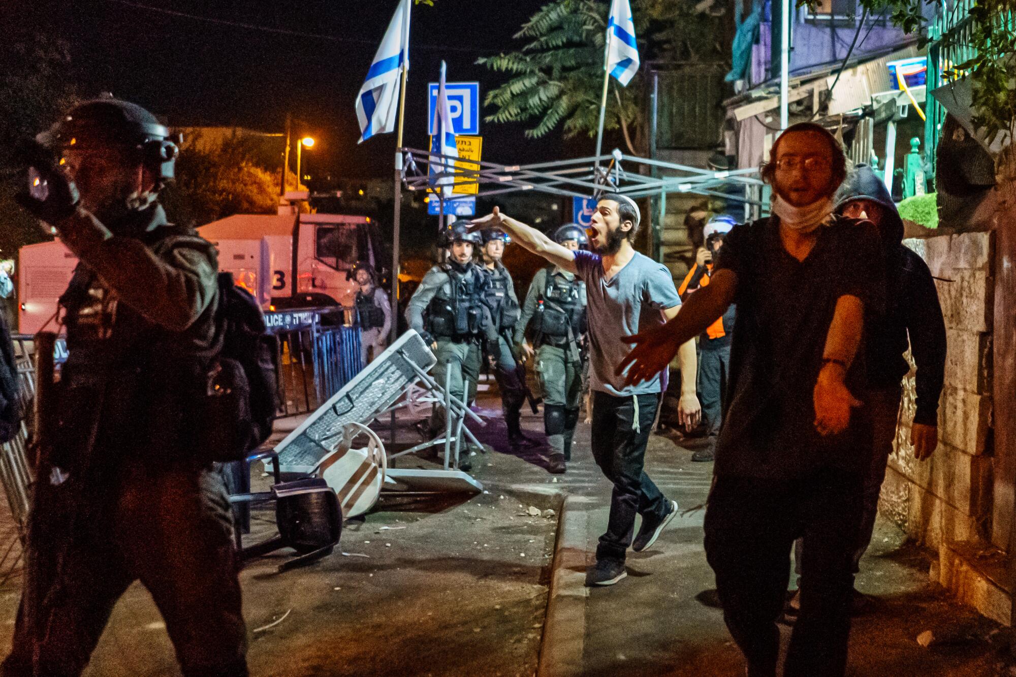 A man shouts in the street as several police officers walk by.