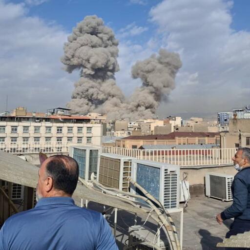 People watch as smoke rises on the skyline after an explosion in Tehran Saturday.