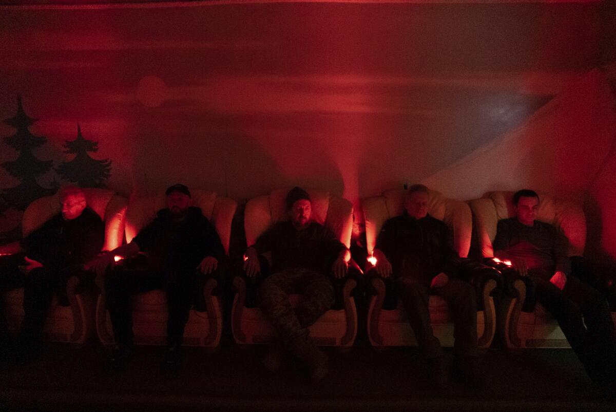 Men sit in easy chairs in a dimly lit room 