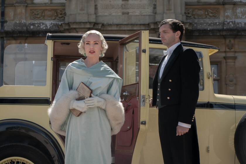 A servant opens a car door for a glamorous woman.