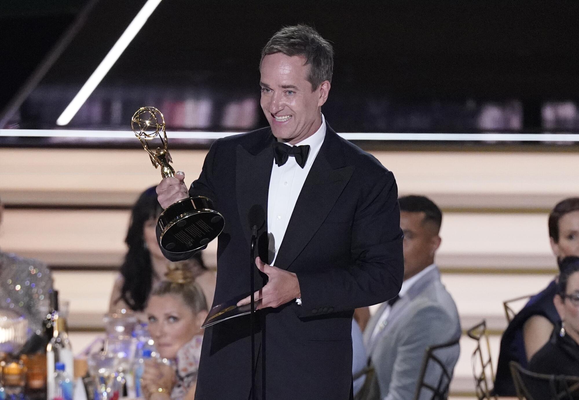 A man smiles as he accepts the Emmy behind a microphone