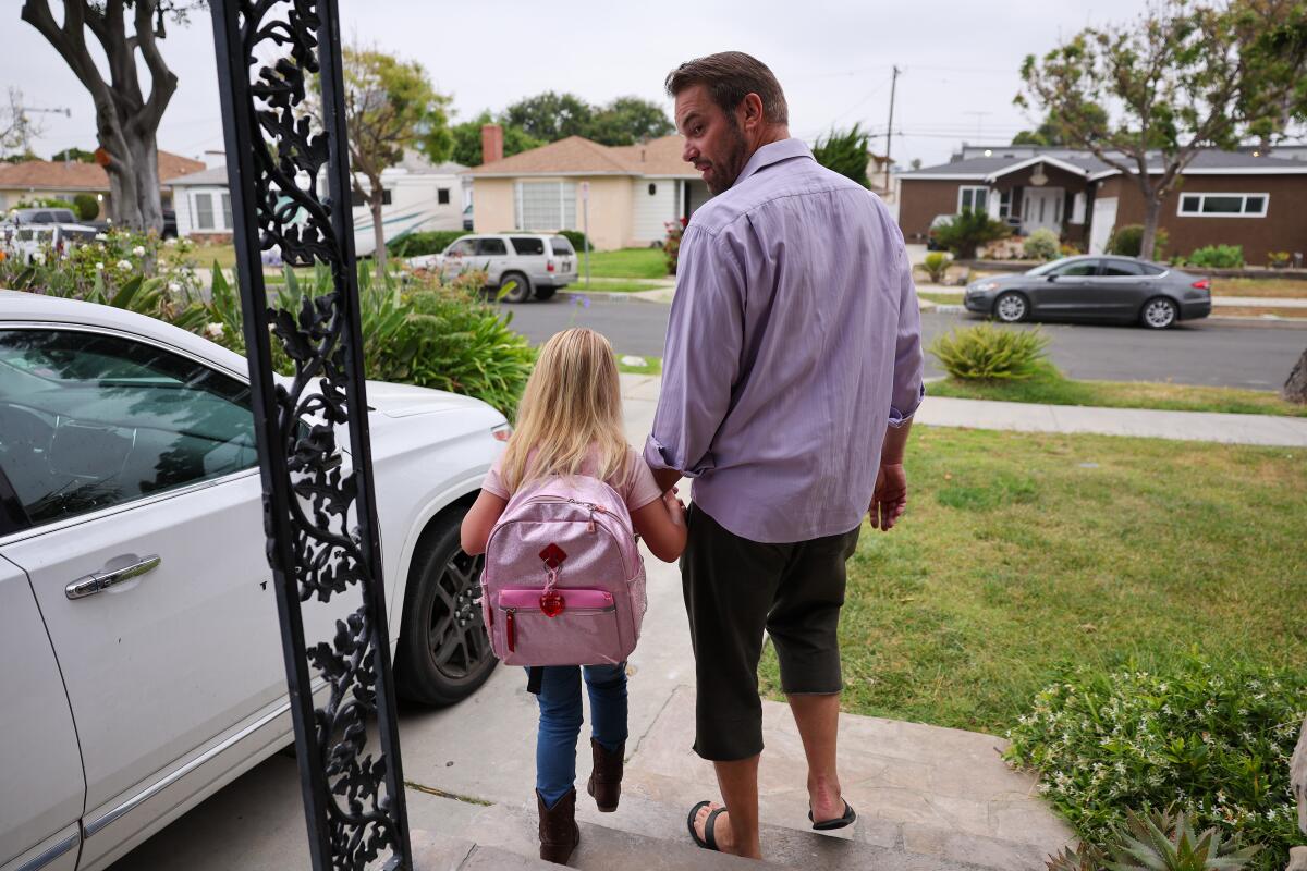 A father holds his daughter's hand as they head out the door for school.