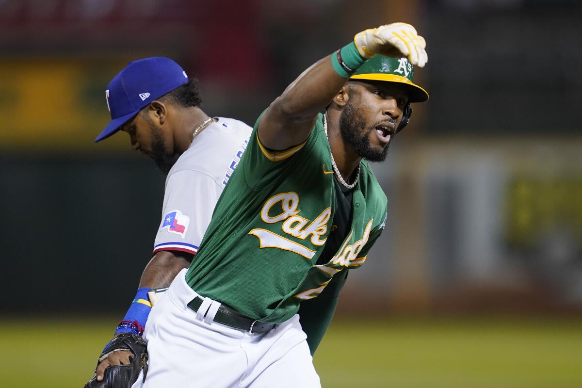 Oakland Athletics' Starling Marte gestures toward teammates after hitting an RBI triple, next to Texas Rangers' Yonny Hernandez during the fourth inning of a baseball game in Oakland, Calif., Friday, Sept. 10, 2021. (AP Photo/Jeff Chiu)