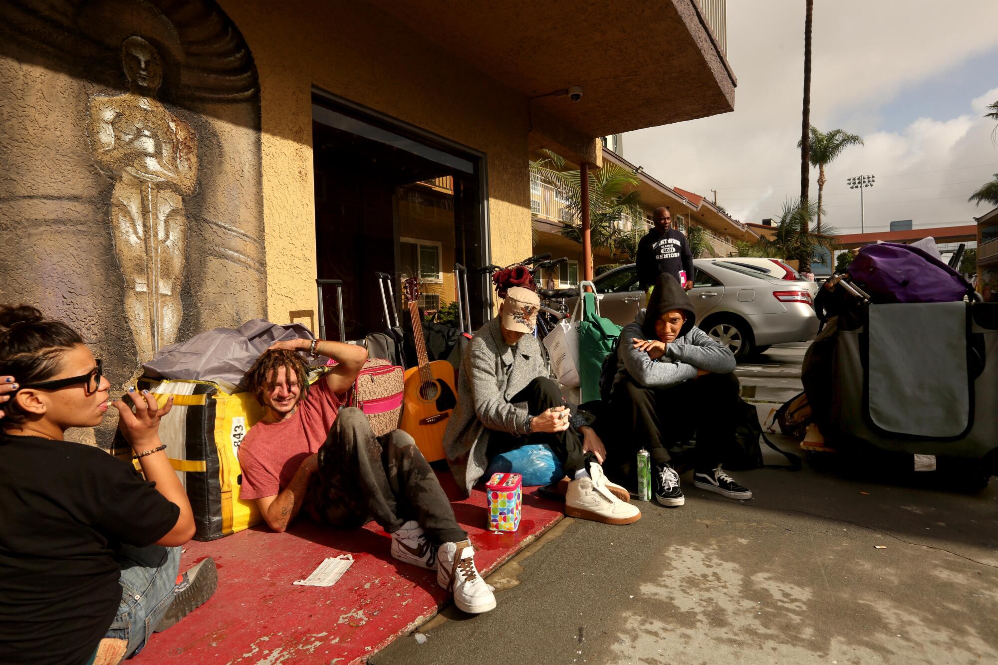 People sit on the ground outside a building with their belongings