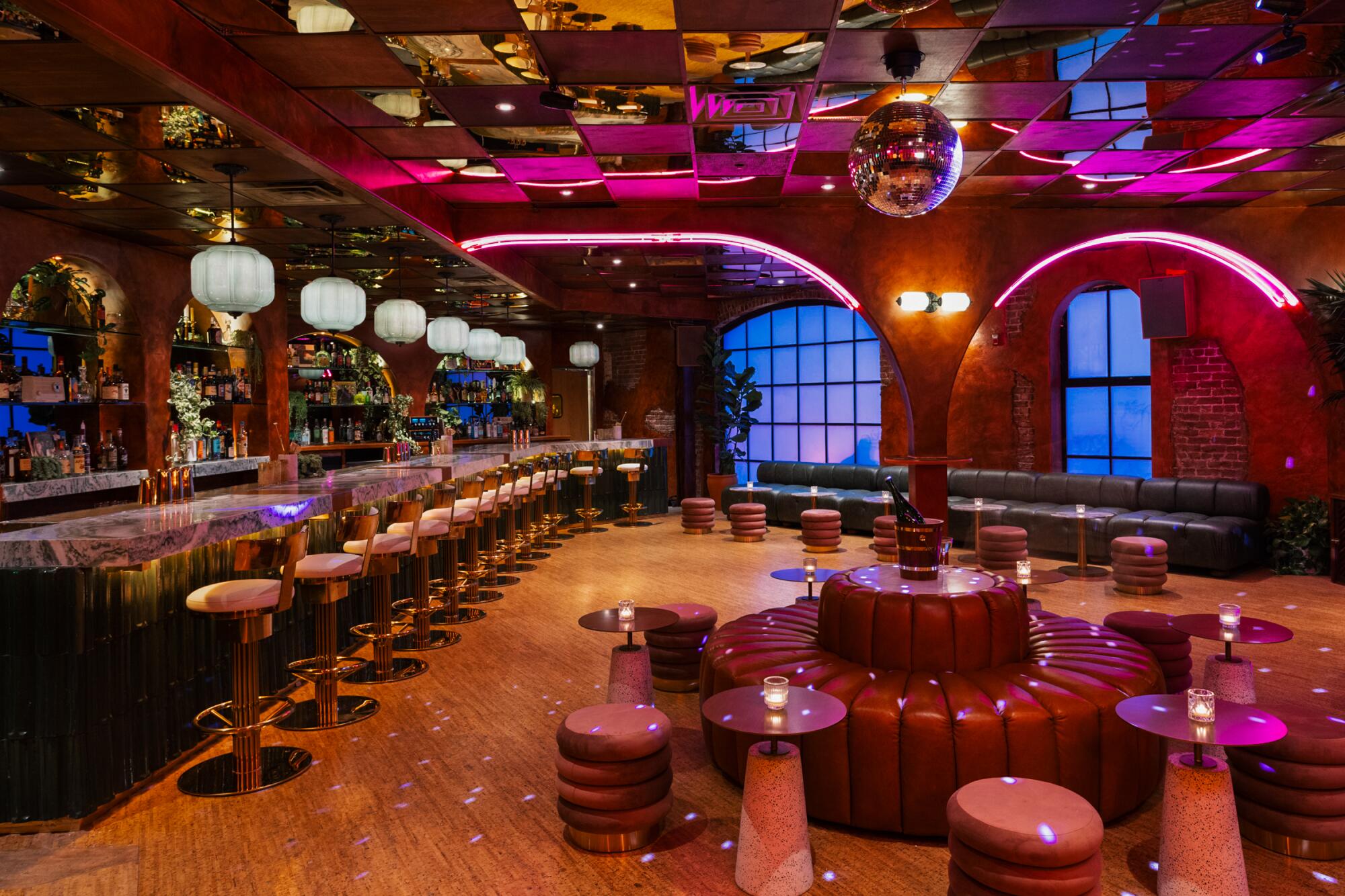 A room with a long bar with barstools and assorted other seating under pink neon