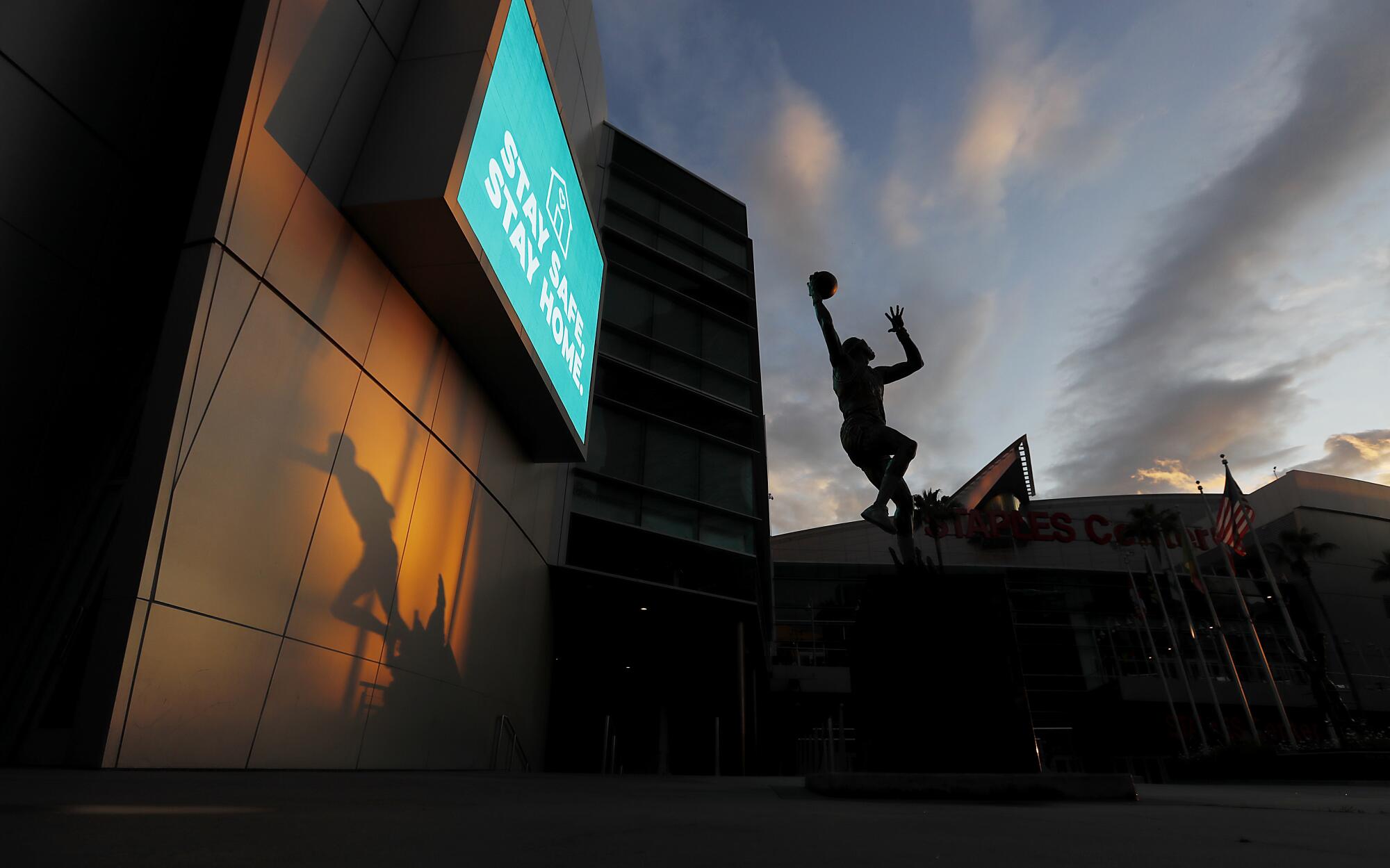 The shadow of a statue of Magic Johnson, left, and a statue of Kareem Abdul Jabbar are frozen in time at Staples Center, where the lights are off and events have been suspended due to the coronavirus pandemic.