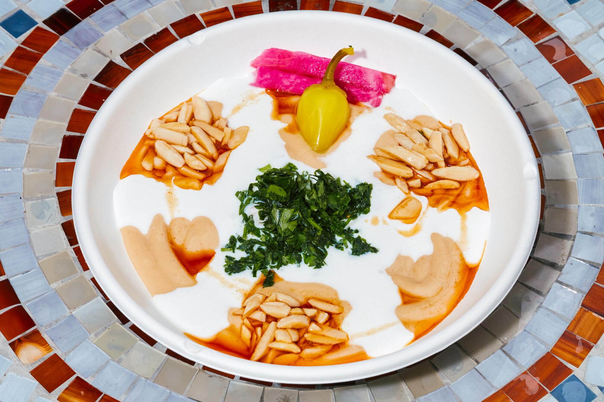 A bowl of fatteh at Nawal -- colorful dollops atop creamy yogurt -- sits on a mosaic table.