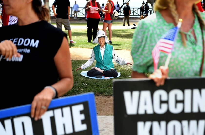 A woman meditates next to a rally opposing COVID-19 vaccination mandates near the Santa Monica Pier.