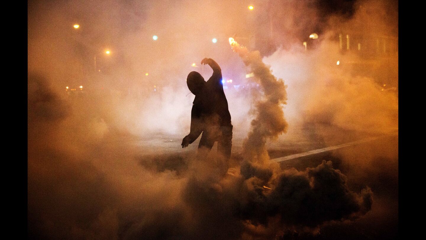 A protester throws a tear gas canister back toward riot police after a 10 p.m. curfew went into effect.
