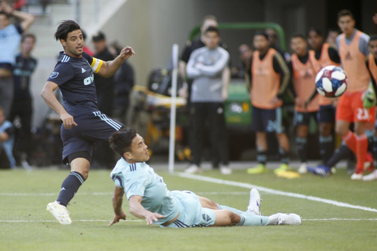 Carlos Vela #10 of Los Angeles FC takes a shot on goal while Kim Kee-Hee #20 of Seattle Sounders slides to block during the second half of a game at Banc of California Stadium on April 21, 2019 in Los Angeles, California.