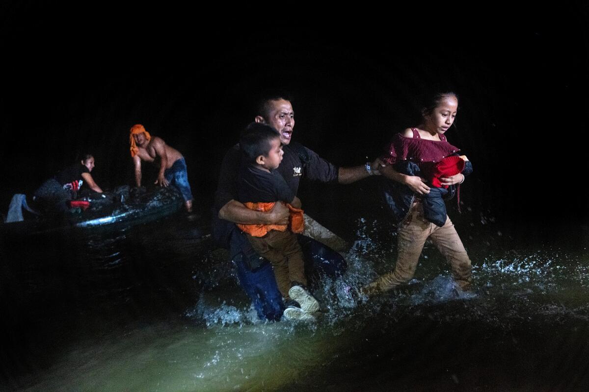 An immigrant father grips his children while walking ashore at the U.S.-Mexico border in Roma, Texas. 