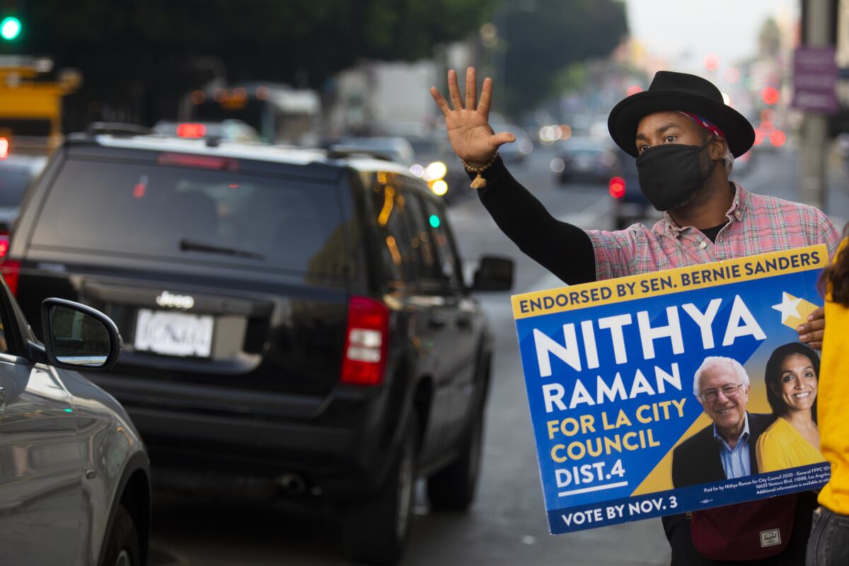 Matthew Gaston holds up a sign for Nithya Raman for L.A. City Council near a voting center at the Wiltern on election day.