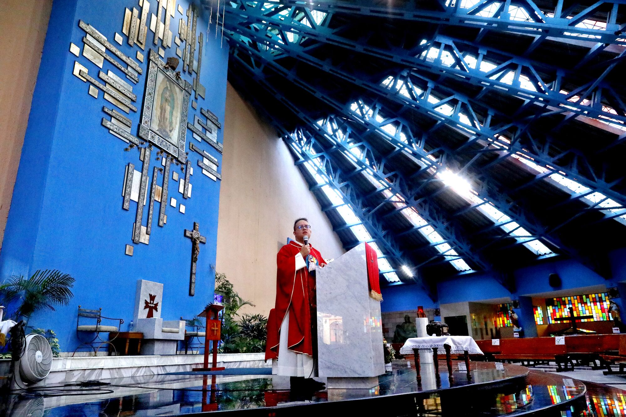 A priest speaks into a microphone in a largely empty church