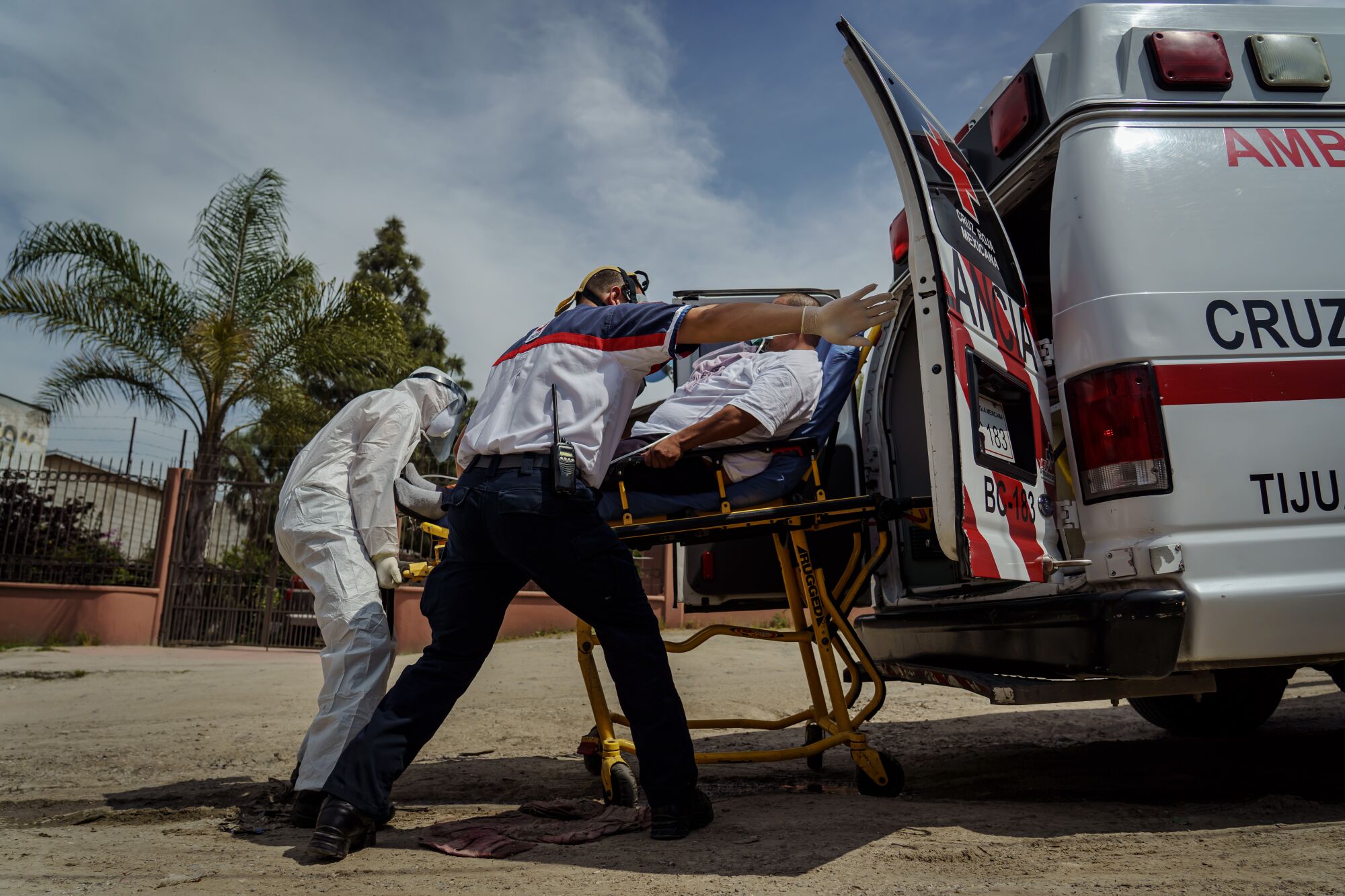 Sergio García abre de par en par la puerta de la ambulancia mientras los paramédicos de la Cruz Roja ayudan a transportar a Eduardo Dionisio Molina, de 41 años, que tiene síntomas relacionados con COVID-19, a un hospital cercano desde su casa en el barrio Ejido Matamoros de Tijuana, México, el 29 de abril de 2020.