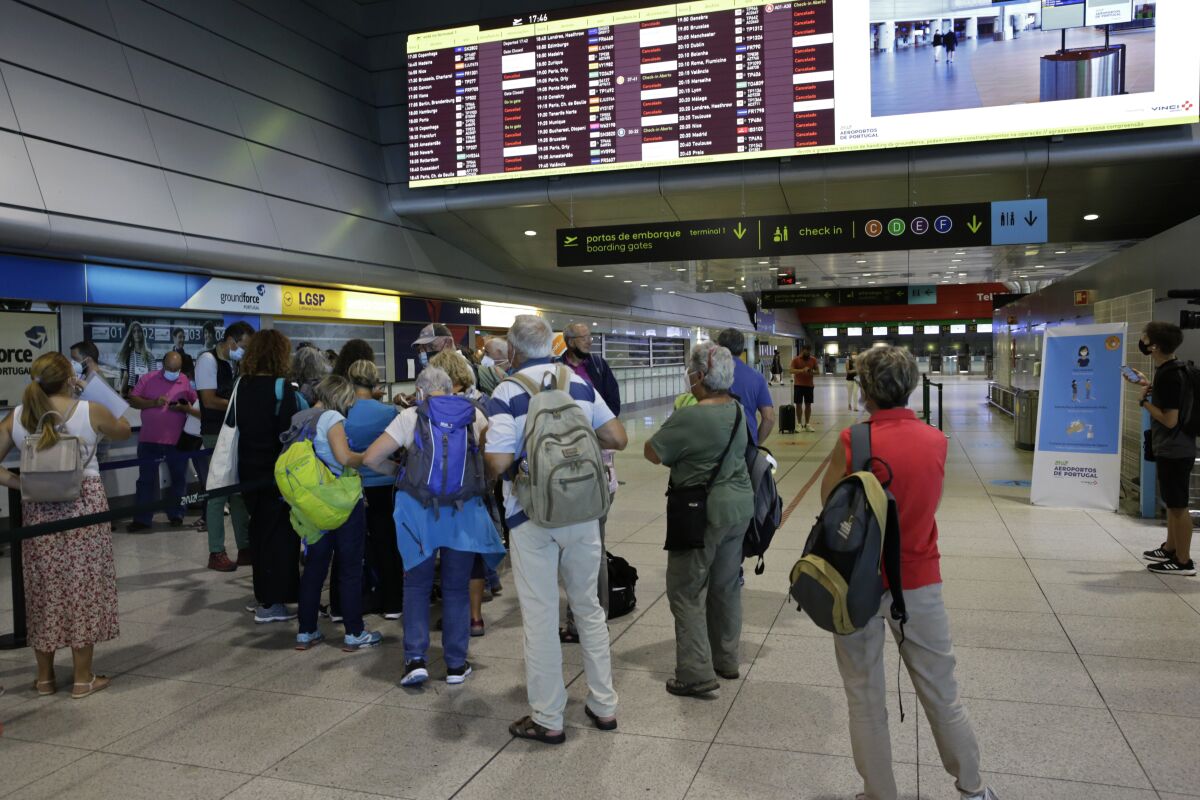 Passengers queue at the counter of Groundforce, a ground handling company at Lisbon airport, beneath a screen showing departing flights Saturday, July 17, 2021. A strike by ground handling workers at Portugal's airports forced the cancellation of over 200 flights on Saturday. The walkouts over wage conditions are scheduled to last through Sunday. (AP Photo/Armando Franca)