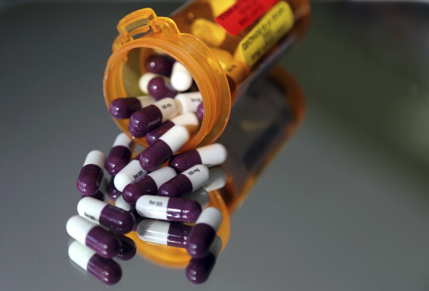 Purple and white drug capsules spill out of a pill bottle.