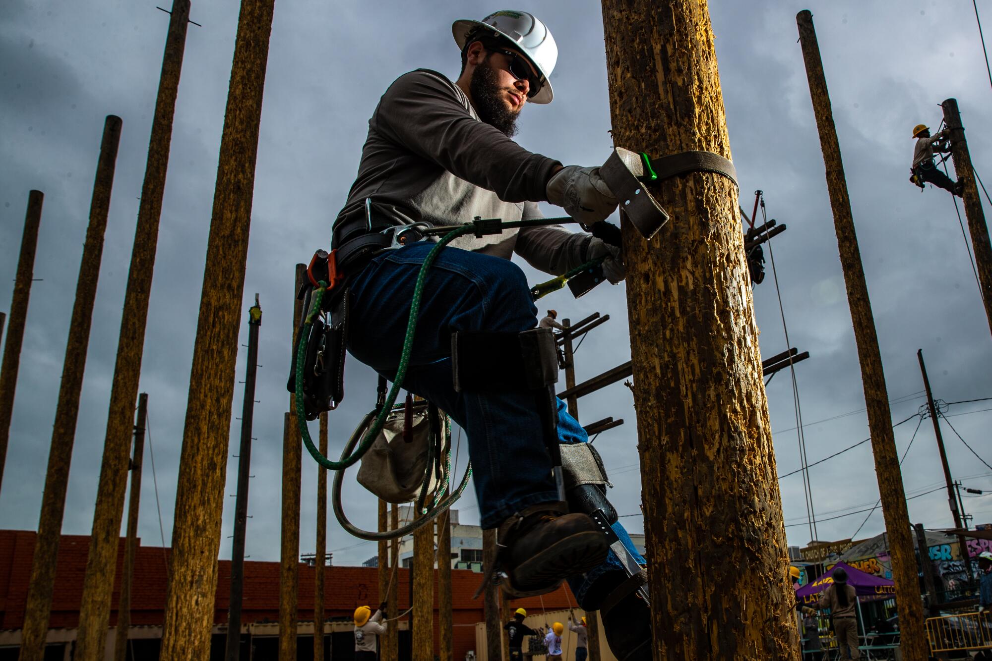 A man in a hardhat climbs a power pole. 