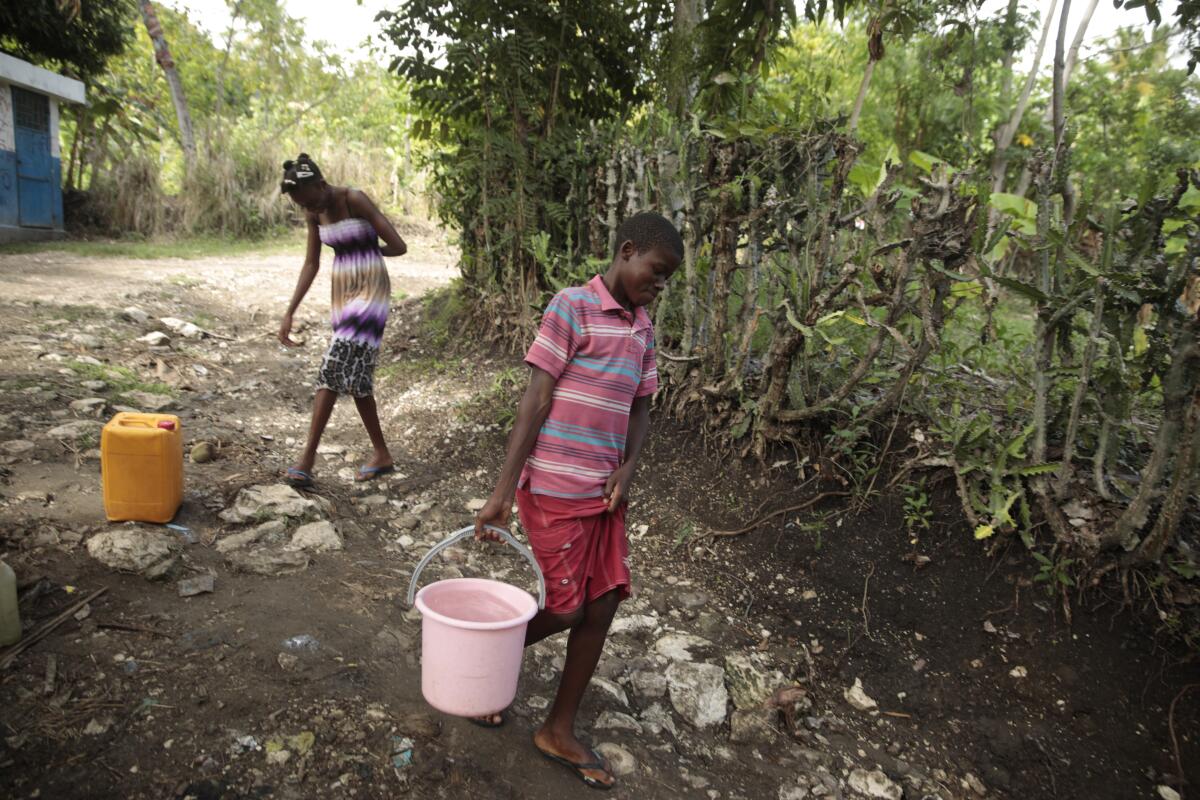 Siblings Mylouise Veillard, left, and Myson walk home with water they collected from a well in a rural Haiti.