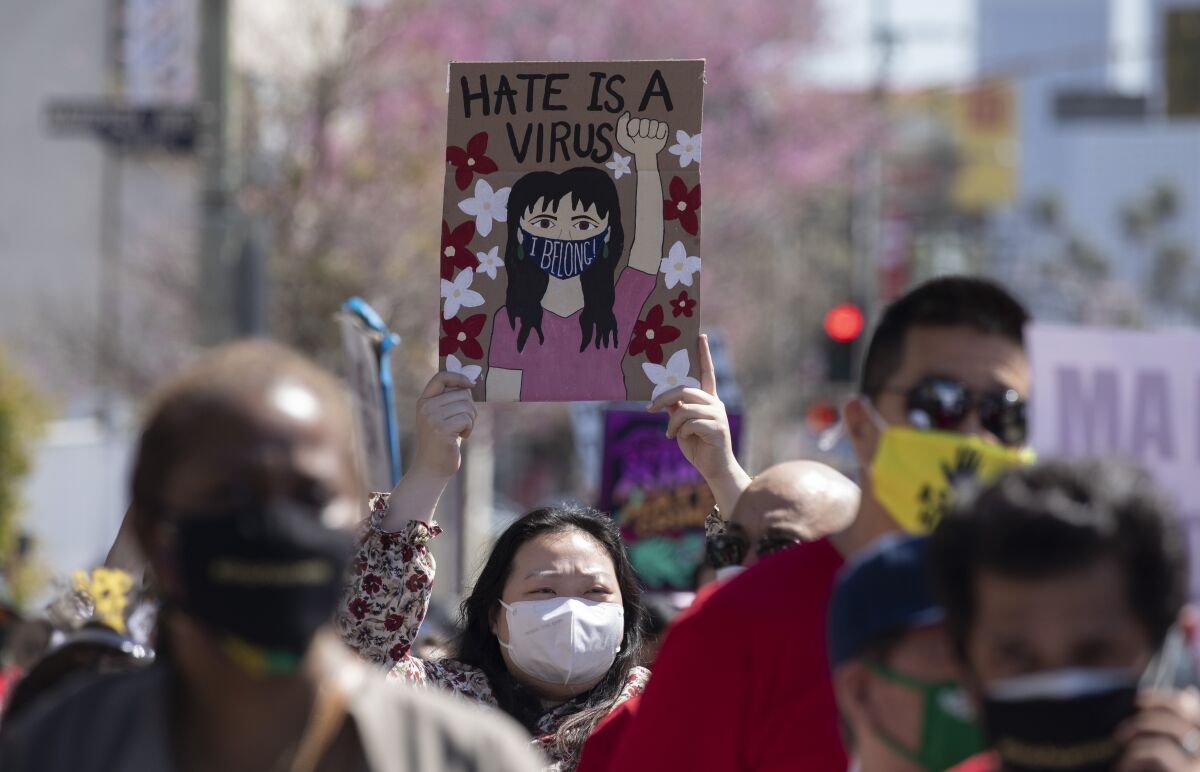 A rally participant holds a sign that reads "Hate is a virus" with a drawing of a person wearing a mask that says "I belong"